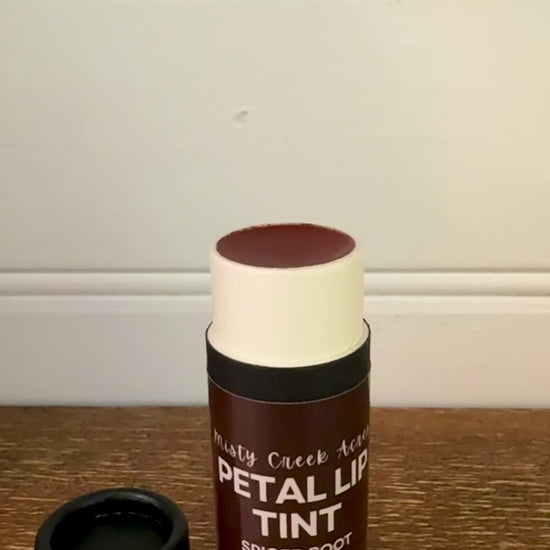 Black cosmetic bottle labeled 'Petals' on a wooden surface with a white wall background