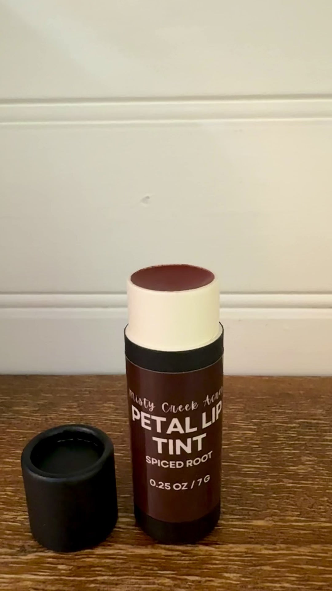 Black cosmetic bottle labeled 'Petals' on a wooden surface with a white wall background