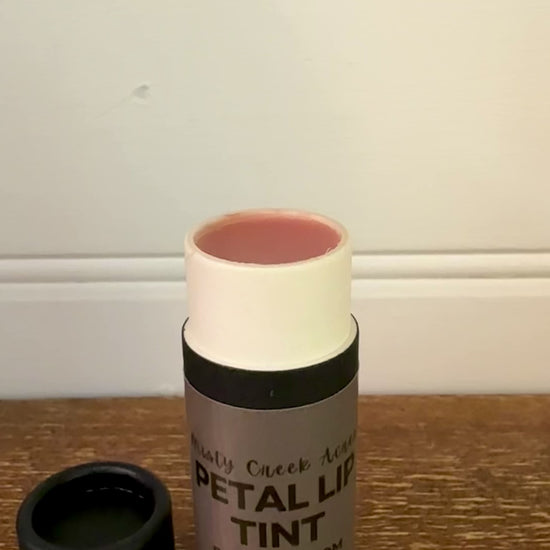 Bottle of petal lip tint on a wooden surface with a white wall background