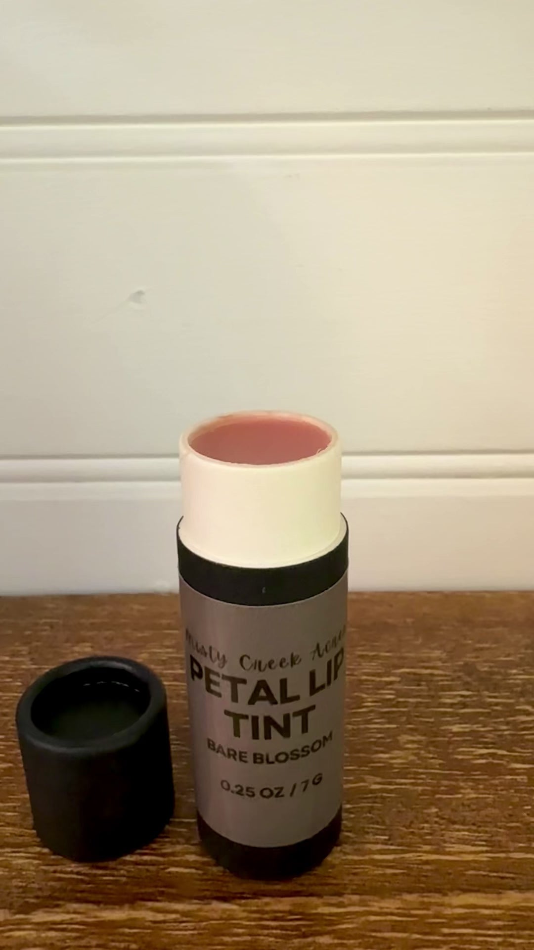 Bottle of petal lip tint on a wooden surface with a white wall background