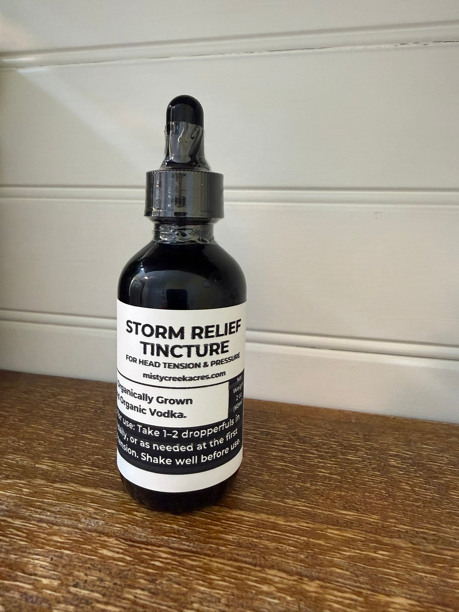 Bottle of Storm Relief Tincture on a wooden surface with a white wall background