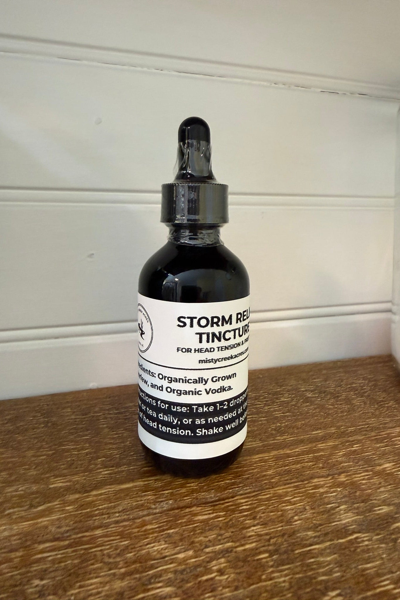 Bottle of Storm Rest Tincture on a wooden surface with a white wall background