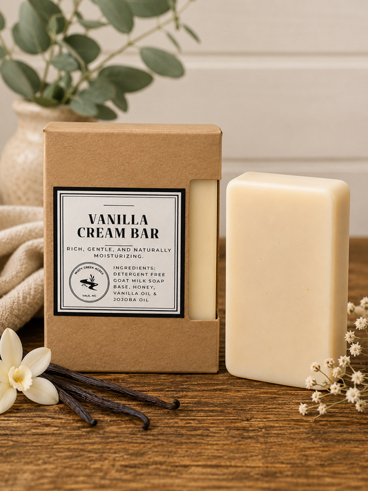 Vanilla cream bar soap with packaging on a wooden surface, surrounded by vanilla beans and flowers.