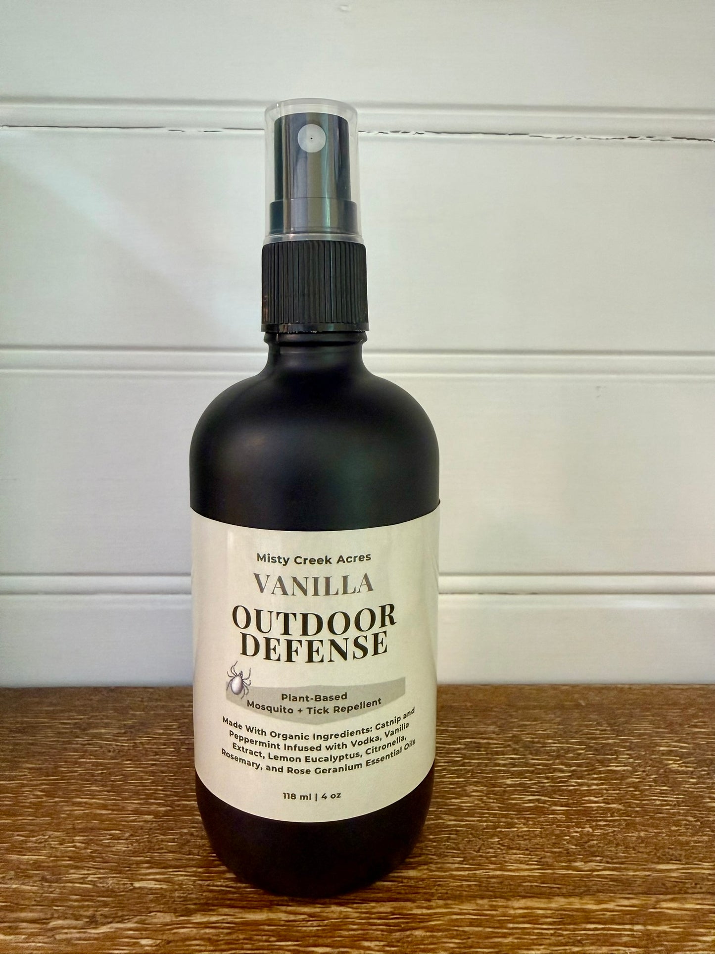 Bottle of Vanilla Outdoor Defense spray on a wooden surface with a white background