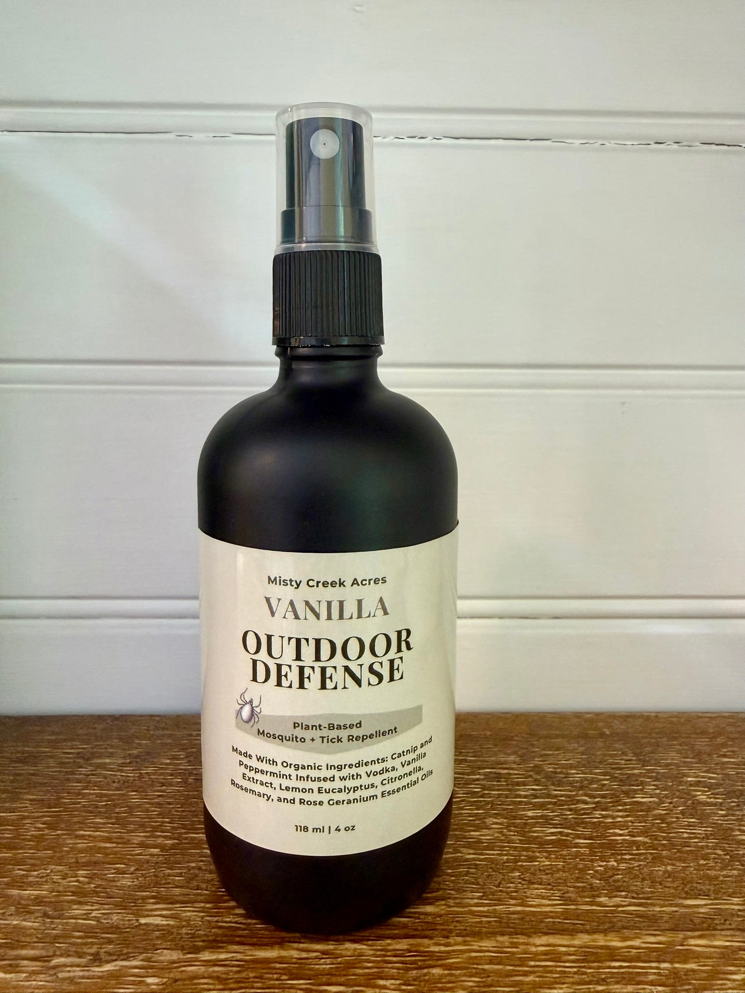 Bottle of Vanilla Outdoor Defense spray on a wooden surface with a white background