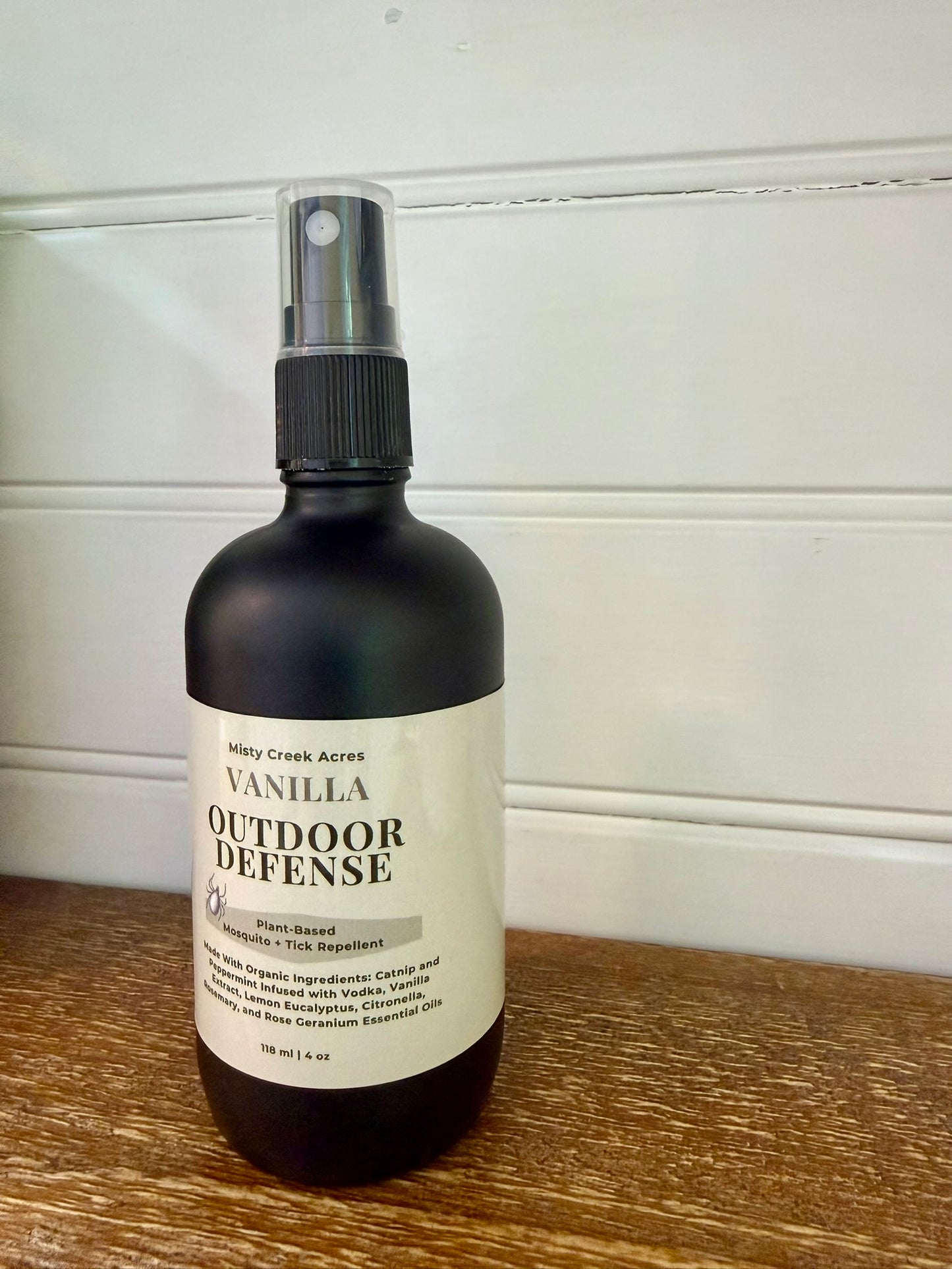 Bottle of Vanilla Outdoor Defense spray on a wooden surface with a white background