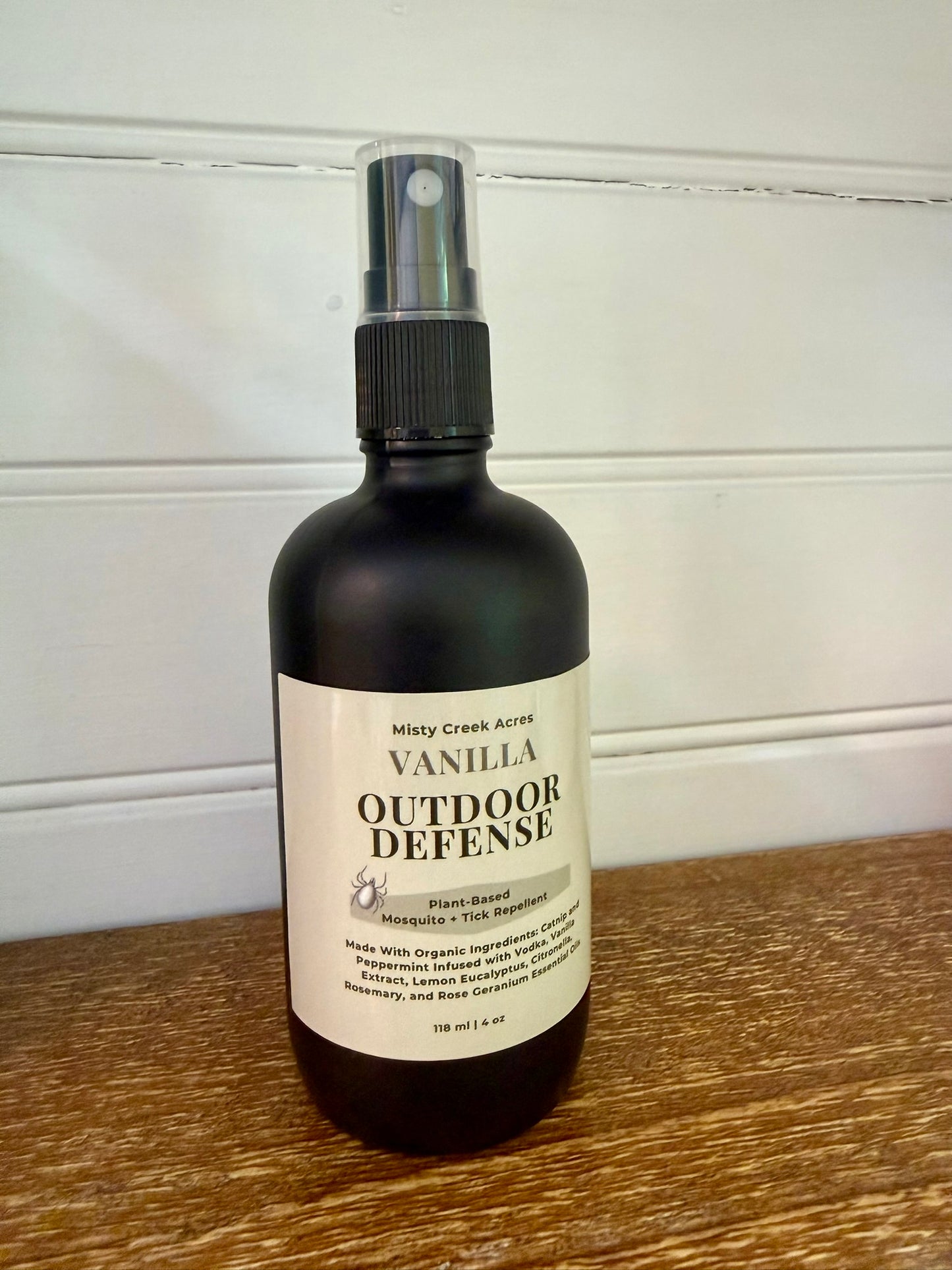 Bottle of Vanilla Outdoor Defense spray on a wooden surface with a white background